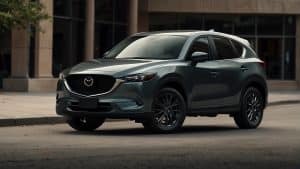 Aerial view of a white Mazda CX-5 parked beside a lake at sunset, capturing the scenic reflection of the car and surrounding nature in the calm waters.